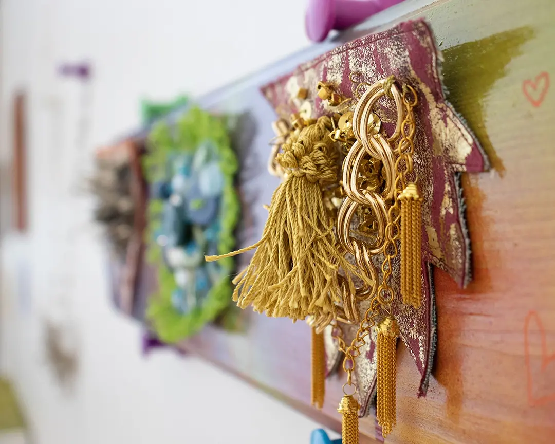 3/4 view of the gold bush mounted on a colorful board. The edges of the bush 
                    are spiked and it has layered gold tassels and chains on it. Two other bushes on the 
                    board are out of focus in the background.