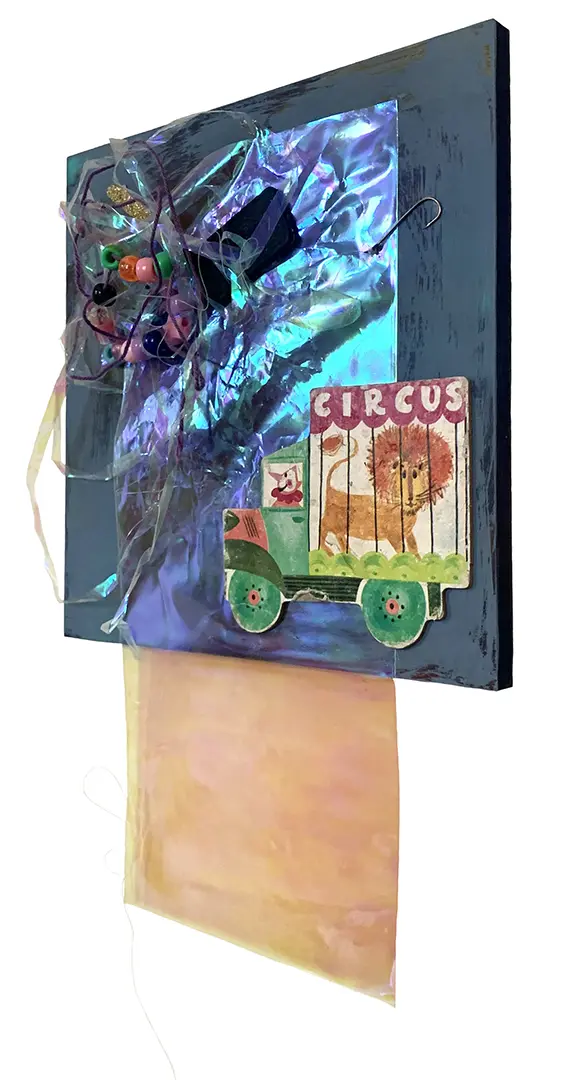 Right angle view of a three-dimensional collage on a painted board. It's made of miscellaneous 
                        trash, including strings of beads, plastic, and a circus cutout from a children's book.