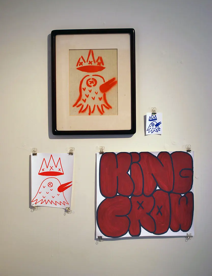 Close up of right wall in photo corner. There's one framed print of a crow with a crown, 
                        a large and small sticker with the same image, and a large sticker that says 'KING CROW'.