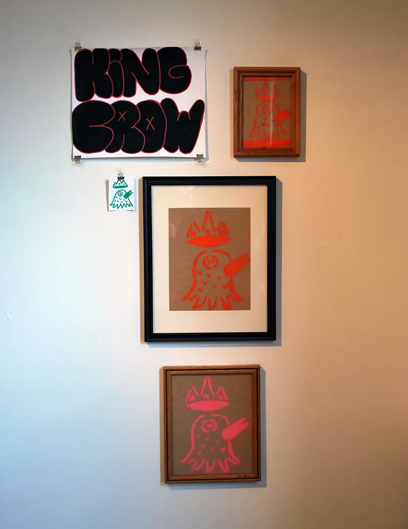 Close up of left wall in photo corner. There's a large format sticker that says 
                        'KING CROW'. There are three framed cardboard prints of a crow with a crown and a small sticker 
                        with the same image.