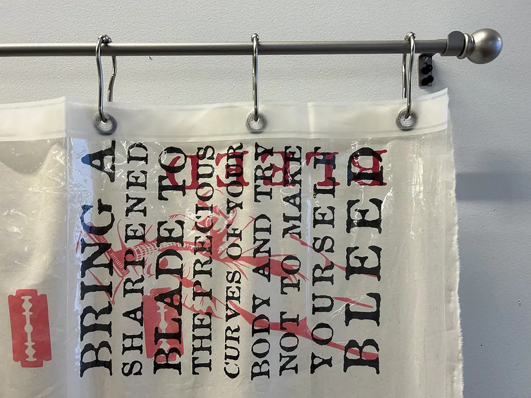 Close up of the top corner of the curtain. The text reads "Bring a sharpened 
                        blade to the precious curves of your body and try not to make yourself bleed." 
                        The text is printed sideways and layered with images of razor blades.