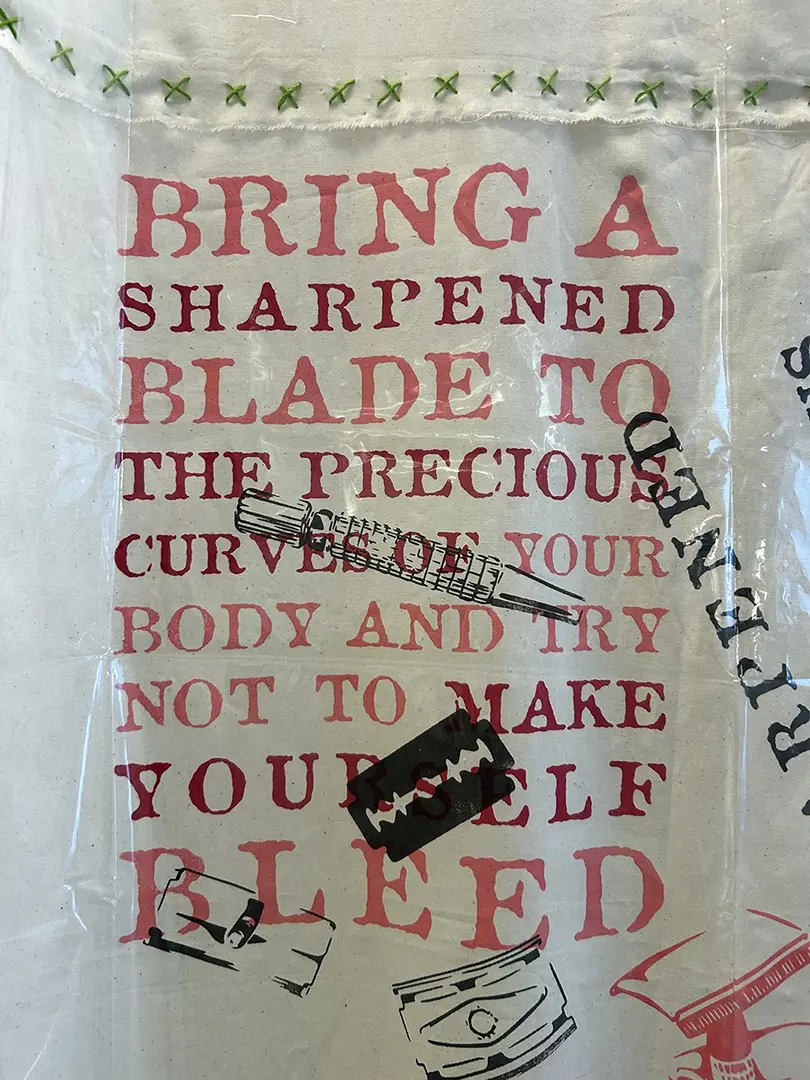 Close up of the curtain with the same printed text. There are green "x" 
                        shaped stitches holding the sections of the muslin curtain together.
