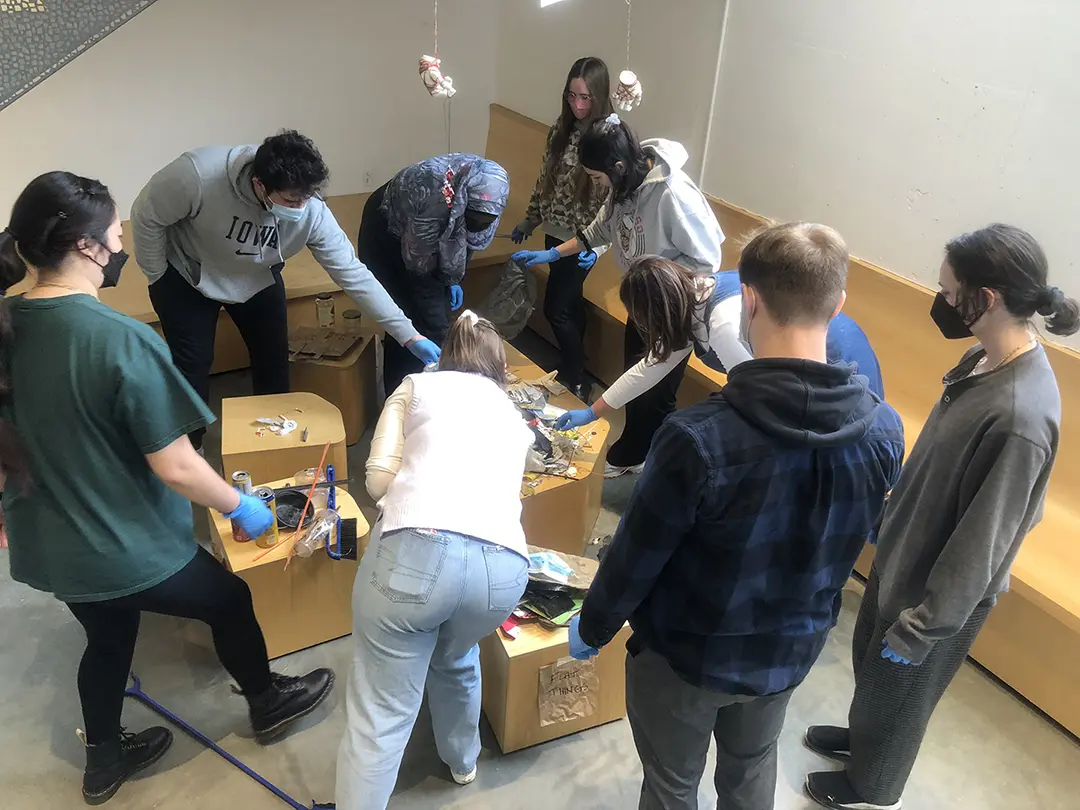 Still from a video of 'Sort Trash With Me!' Kate and their classmates are 
                    sorting trash that has been dumped on a pedestal in the Visual Arts Building.