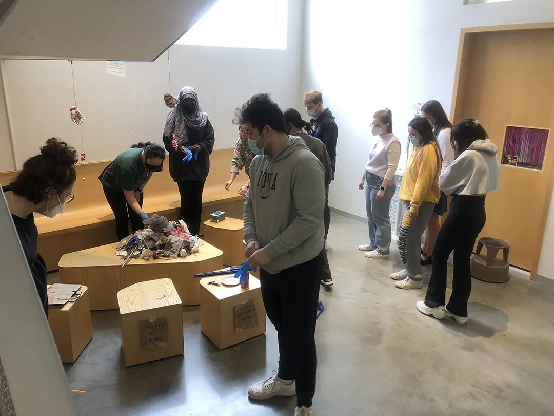 Still from a video of 'Sort Trash With Me!' Kate and their classmates are 
                    sorting trash that has been dumped on a pedestal in the Visual Arts Building.